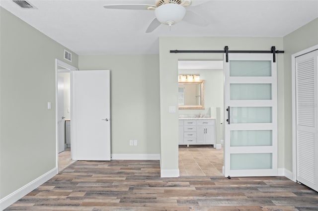 unfurnished bedroom featuring connected bathroom, a barn door, hardwood / wood-style floors, and a closet