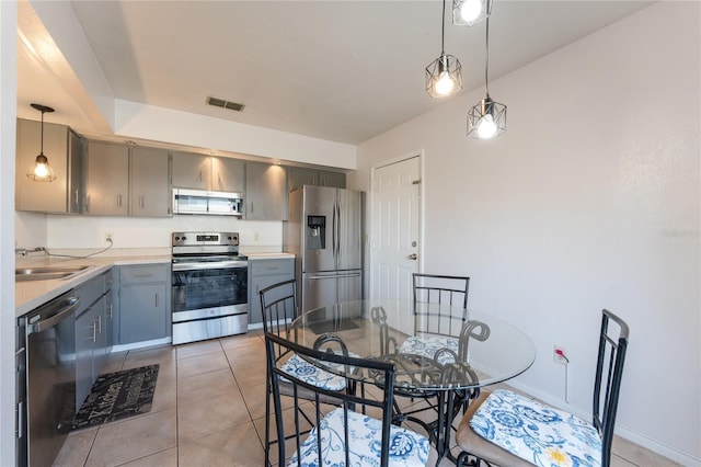 kitchen with appliances with stainless steel finishes, decorative light fixtures, sink, gray cabinetry, and light tile patterned floors