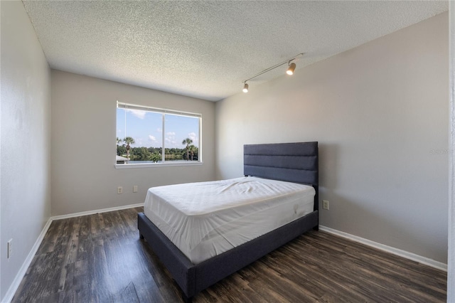 bedroom with dark hardwood / wood-style flooring, track lighting, and a textured ceiling