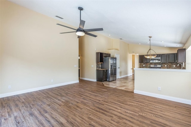 unfurnished living room with high vaulted ceiling, light wood-type flooring, sink, and ceiling fan