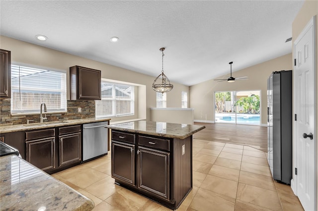 kitchen featuring appliances with stainless steel finishes, decorative light fixtures, sink, a center island, and light stone counters