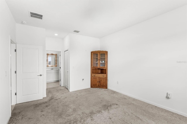 unfurnished bedroom with a closet, light colored carpet, and ensuite bath