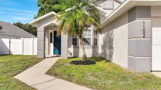 property entrance featuring a lawn, fence, an attached garage, and stucco siding