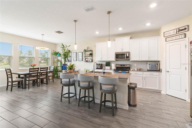 kitchen with appliances with stainless steel finishes, a breakfast bar area, decorative light fixtures, white cabinetry, and a kitchen island with sink