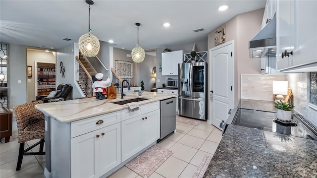 kitchen featuring stainless steel appliances, white cabinetry, a sink, an island with sink, and exhaust hood