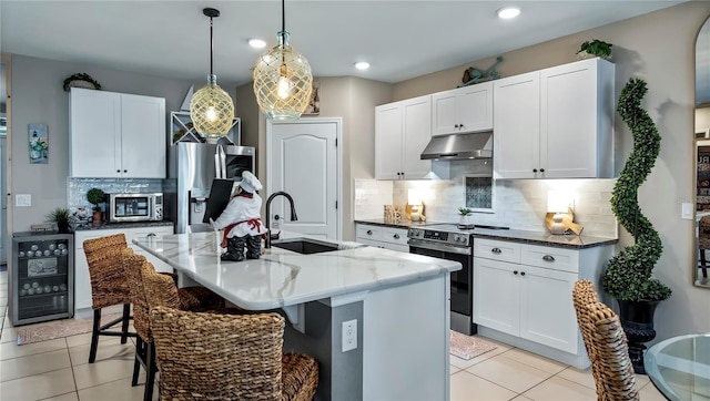 kitchen with wine cooler, stainless steel appliances, hanging light fixtures, an island with sink, and under cabinet range hood