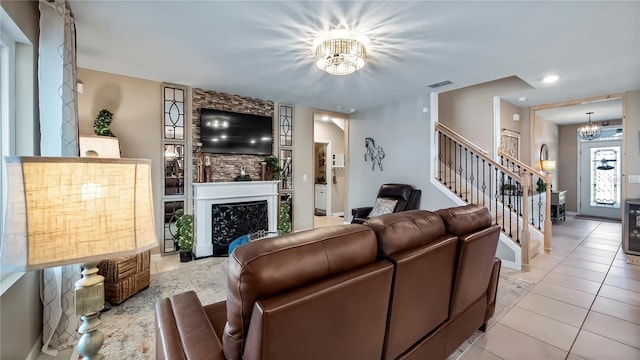 living area featuring light tile patterned floors, visible vents, stairway, a fireplace, and a notable chandelier