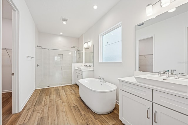 full bath featuring a walk in closet, visible vents, a sink, a shower stall, and wood finished floors