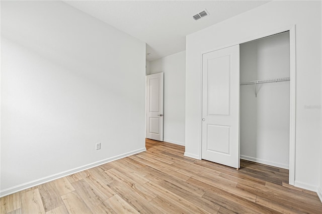 unfurnished bedroom featuring light wood finished floors, baseboards, visible vents, and a closet