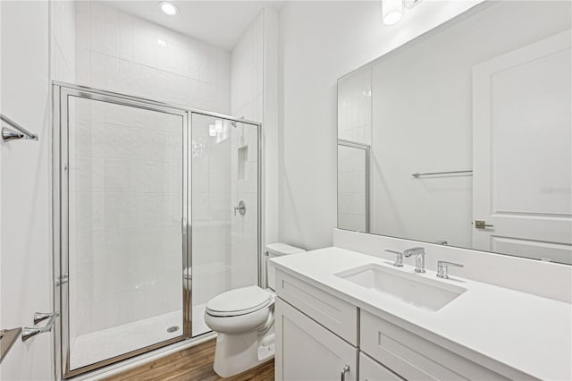 bathroom with toilet, a shower stall, wood finished floors, and vanity