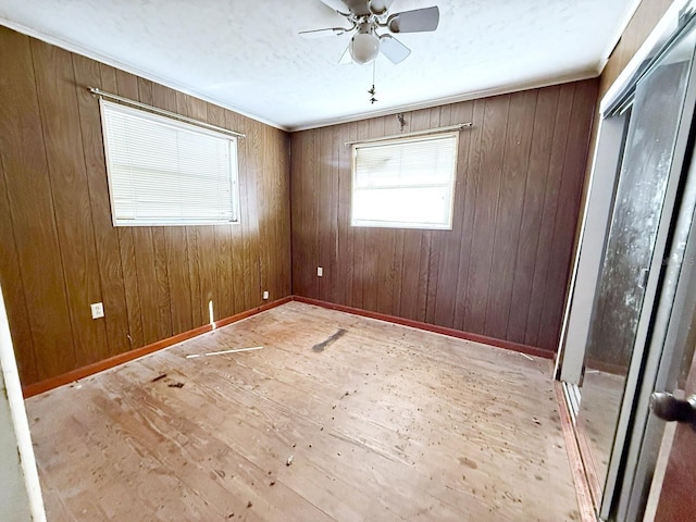 empty room featuring crown molding, wood walls, ceiling fan, and light hardwood / wood-style flooring