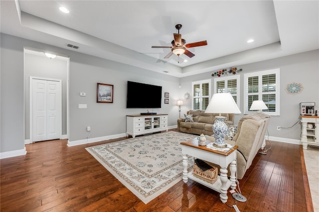 living room featuring baseboards, visible vents, a raised ceiling, and dark wood-style flooring