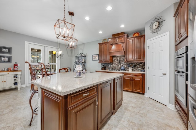 kitchen featuring light stone counters, brown cabinets, oven, hanging light fixtures, and a center island