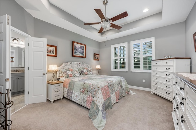 bedroom with light carpet, a tray ceiling, a sink, and baseboards