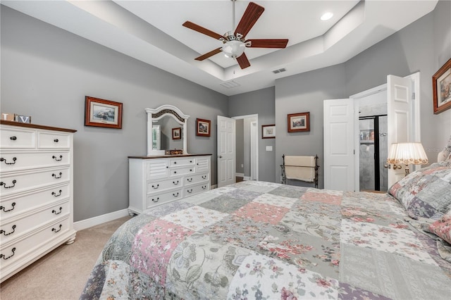 bedroom with light carpet, visible vents, baseboards, ceiling fan, and a tray ceiling