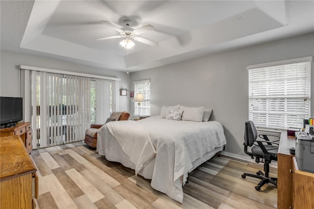 bedroom with ceiling fan, light hardwood / wood-style flooring, access to outside, and a raised ceiling