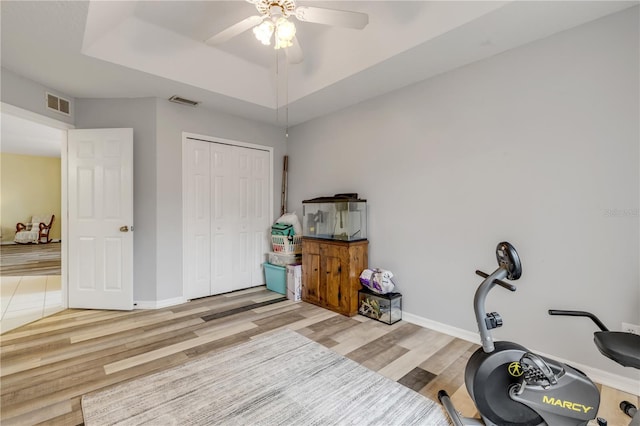 exercise room featuring light hardwood / wood-style flooring, ceiling fan, and a raised ceiling