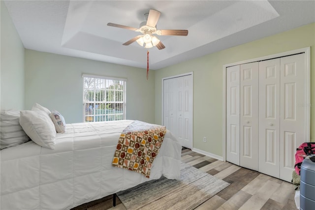 bedroom featuring ceiling fan, light hardwood / wood-style flooring, a raised ceiling, and two closets