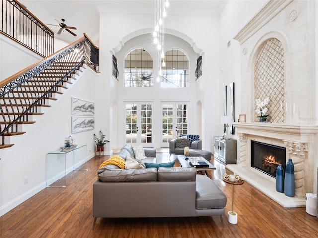 living room featuring hardwood / wood-style floors, a high ceiling, a high end fireplace, ceiling fan with notable chandelier, and french doors