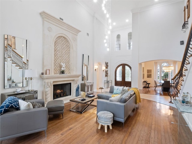 living room with a towering ceiling, hardwood / wood-style floors, ornamental molding, a premium fireplace, and french doors