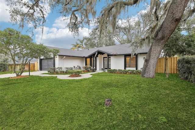 mid-century inspired home featuring a garage, concrete driveway, fence, a front yard, and stucco siding