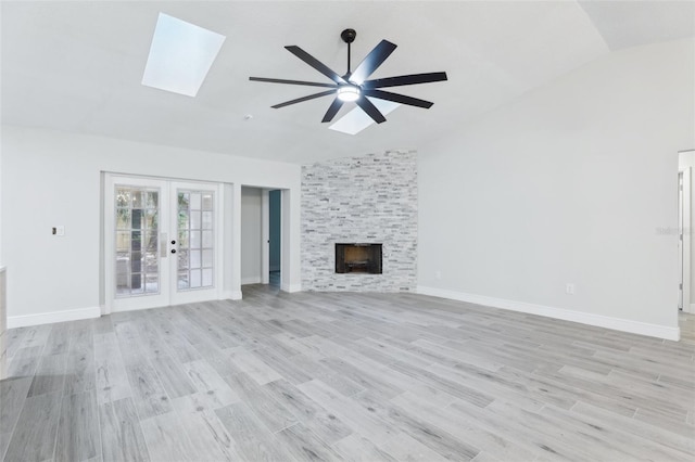 unfurnished living room featuring french doors, lofted ceiling, a large fireplace, light wood-type flooring, and baseboards