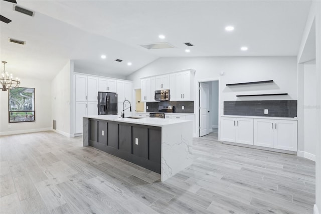 kitchen with a kitchen island with sink, stainless steel appliances, a sink, white cabinetry, and vaulted ceiling