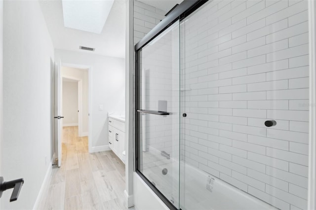 bathroom with baseboards, visible vents, shower / bath combination with glass door, wood finished floors, and vanity