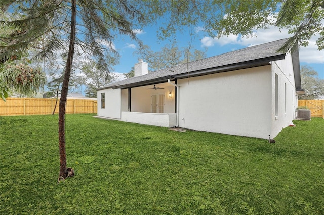 back of property featuring a ceiling fan, a chimney, fence, a yard, and stucco siding