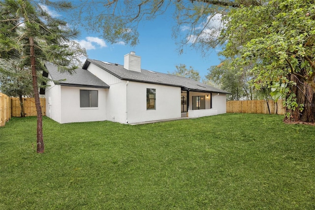 back of property featuring a fenced backyard, a chimney, a lawn, and roof with shingles