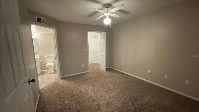 unfurnished bedroom with ceiling fan, carpet flooring, connected bathroom, a textured ceiling, and a spacious closet