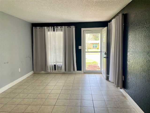 unfurnished room with a textured wall, baseboards, a textured ceiling, and light tile patterned flooring