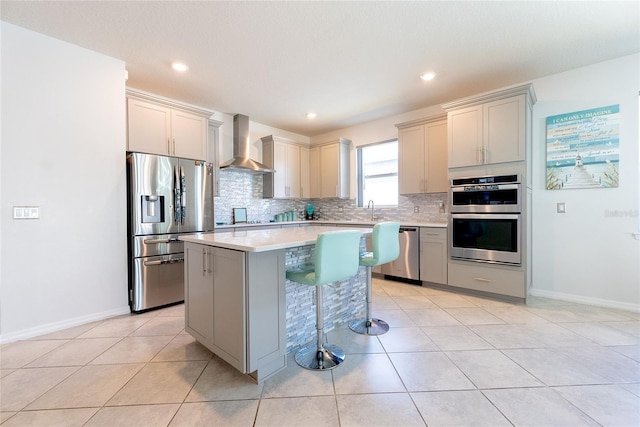 kitchen featuring a kitchen island, tasteful backsplash, light tile patterned floors, stainless steel appliances, and wall chimney range hood