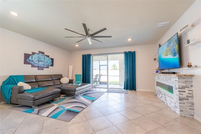 living room featuring ceiling fan, a stone fireplace, and light tile patterned floors