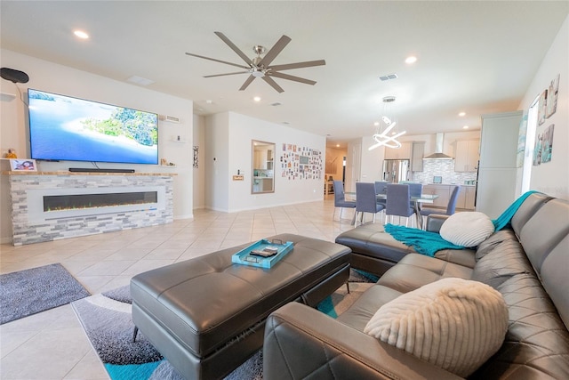 tiled living room featuring a stone fireplace and ceiling fan with notable chandelier