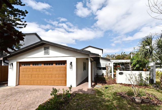 view of front of home with decorative driveway, an attached garage, fence, and stucco siding