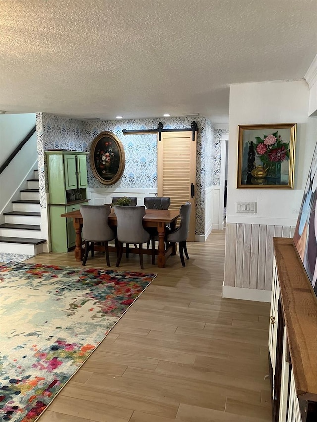 1611 Chestnut Ave, Winter Park, FL 32789 - dining space featuring wallpapered walls, a barn door, a textured ceiling, stairs, and light wood finished floors