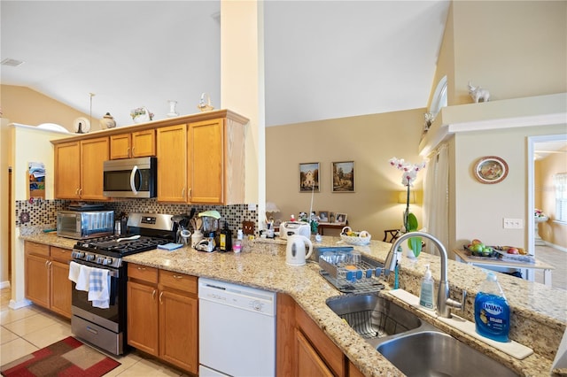 kitchen featuring light tile patterned floors, a sink, vaulted ceiling, appliances with stainless steel finishes, and tasteful backsplash