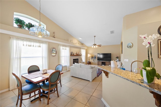 dining area featuring visible vents, light tile patterned flooring, a tiled fireplace, and ceiling fan with notable chandelier