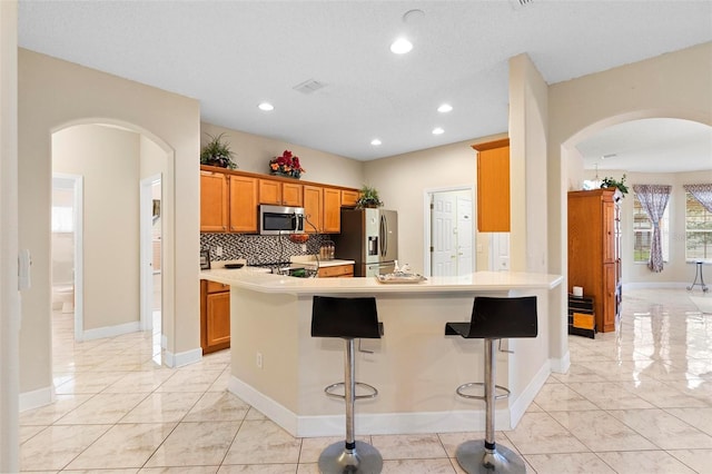 kitchen with arched walkways, a breakfast bar, decorative backsplash, appliances with stainless steel finishes, and a peninsula