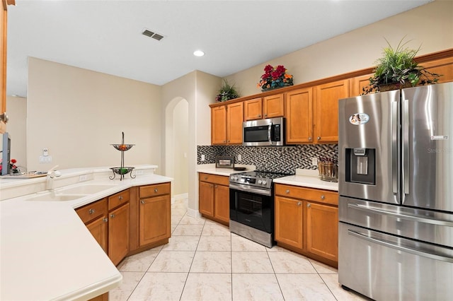 kitchen with arched walkways, visible vents, brown cabinets, stainless steel appliances, and a sink