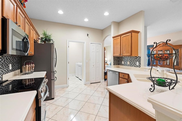 kitchen with washer / dryer, arched walkways, brown cabinets, stainless steel appliances, and light countertops