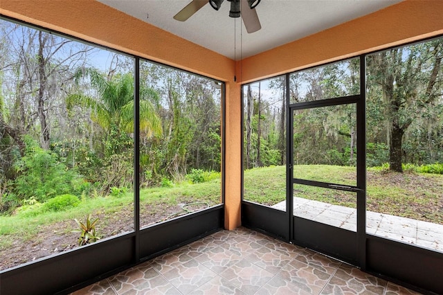 unfurnished sunroom with a ceiling fan and a forest view