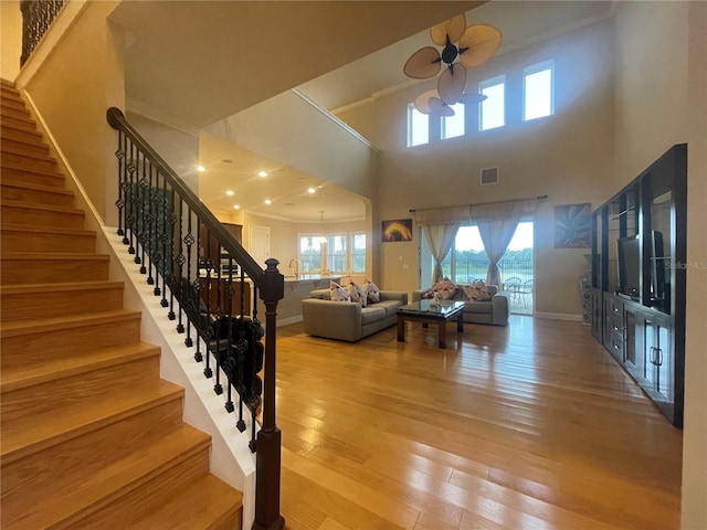 living area with visible vents, a towering ceiling, stairway, wood finished floors, and baseboards