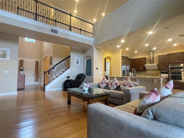 living room featuring arched walkways, visible vents, light wood-style flooring, a towering ceiling, and stairs