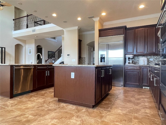 kitchen with arched walkways, a kitchen island, light stone countertops, stainless steel appliances, and backsplash