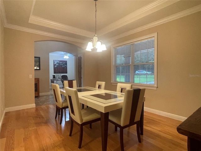 dining room with arched walkways, a raised ceiling, baseboards, and wood finished floors