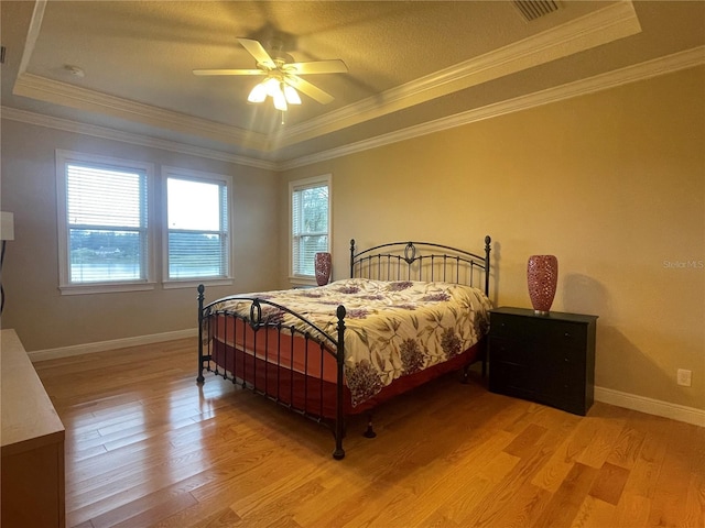 bedroom featuring ornamental molding, a raised ceiling, and light wood-style floors