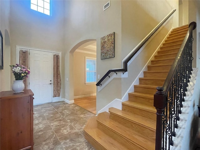 entrance foyer featuring arched walkways, crown molding, visible vents, a towering ceiling, and baseboards