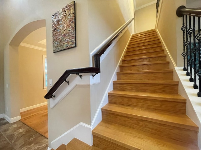 stairway featuring baseboards, arched walkways, wood finished floors, and ornamental molding